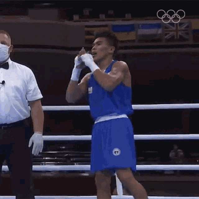 a man in a blue boxing uniform is standing in a ring with a referee