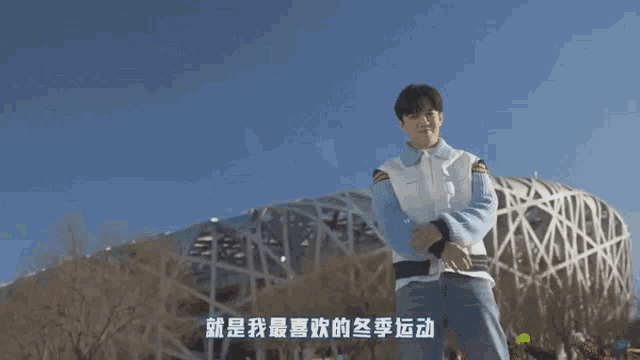 a man in a blue sweater stands in front of a building with chinese writing