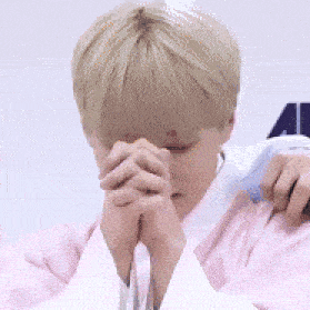 a man in a pink shirt and white shirt is praying with his hands folded in front of his face .