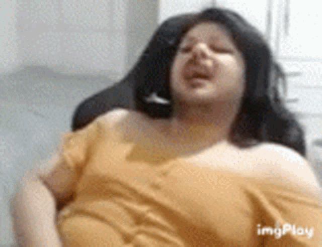 a woman in a yellow shirt is sitting in a chair with her eyes closed and her mouth open .