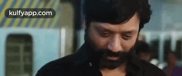 a man with a beard is standing in front of a train with his eyes closed .