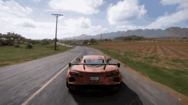 a red sports car is driving down a road with mountains behind it