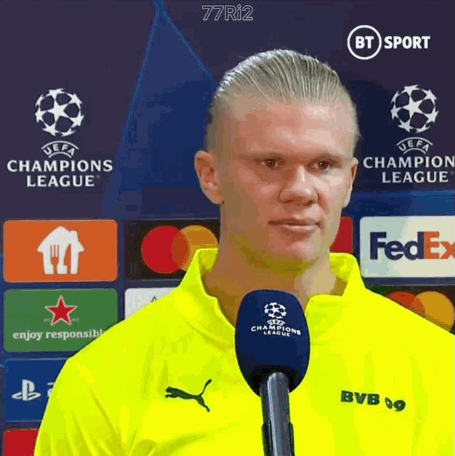 a man in a yellow shirt is talking into a microphone with fedex in the background