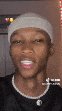 a man wearing a white beanie and a pearl necklace has a tiktok sticker on his face