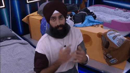 a man with a beard wearing a turban is standing in front of a giant cheese