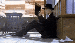a man in a fedora is sitting on the floor reading a book