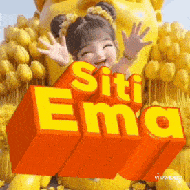 a little girl is standing in front of a yellow statue with the words " siti ema " on it