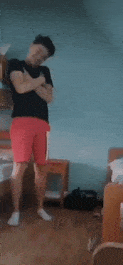 a man in a black shirt and red shorts is standing on one leg in a room .
