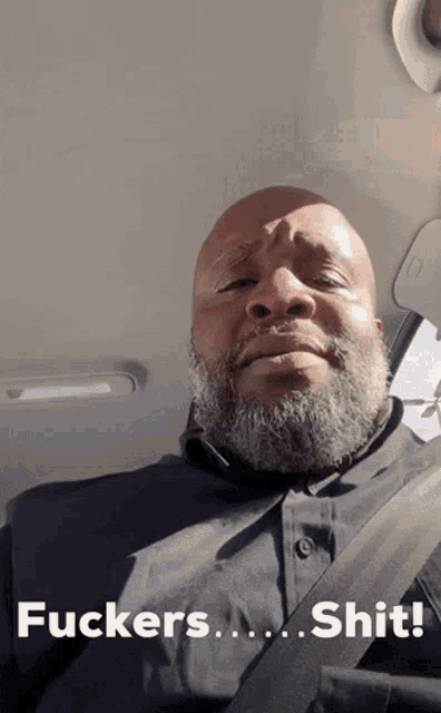 a bald man with a beard is sitting in a car with the words " fuckers shit " on the bottom