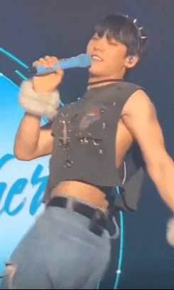 a man is singing into a microphone on stage while wearing a crop top .