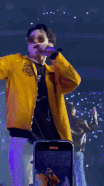a man in a yellow jacket is singing into a microphone on stage