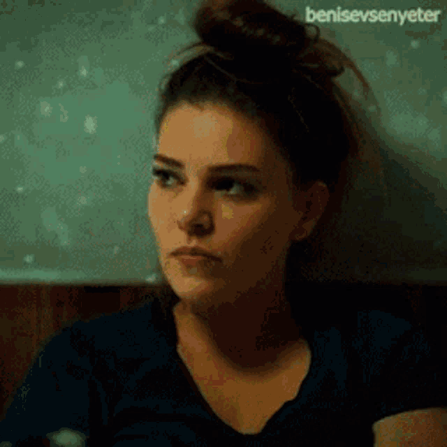 a woman with her hair in a bun is making a funny face while wearing a blue shirt .