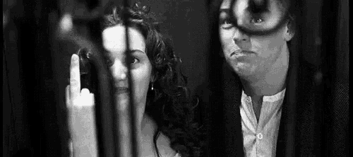 a man and woman are standing next to each other in a black and white photo . the woman is giving the middle finger .
