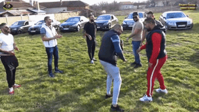 a group of men are standing in a field with cars parked in the background .