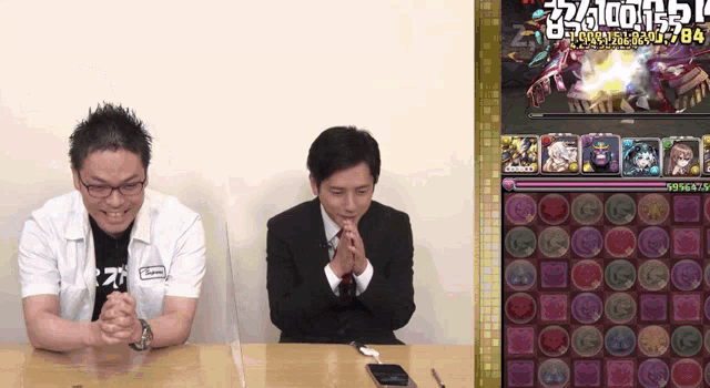 two men are sitting at a table with their hands folded in front of a screen that has the number 2764 on the top