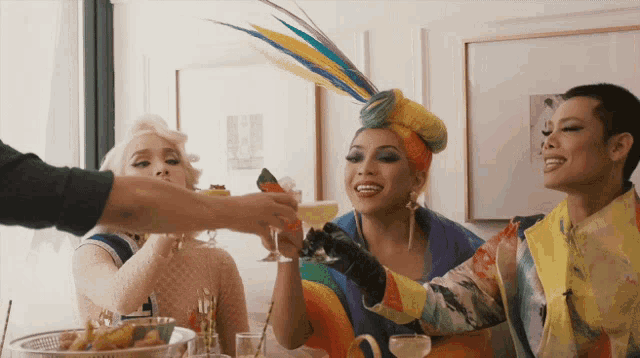 a woman with a feathered headband is toasting with two other women