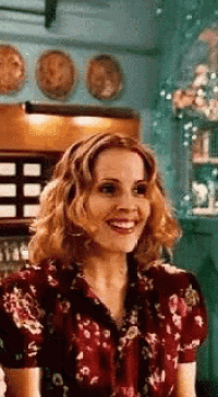 a woman in a red floral shirt is smiling in a room with plates on the wall .