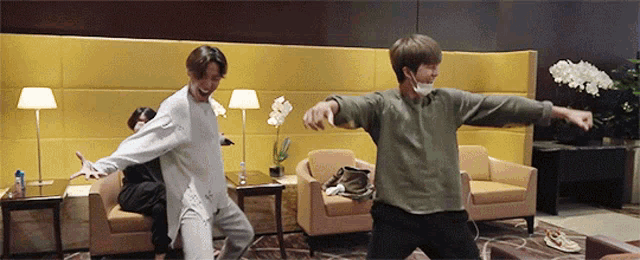 two men are dancing in a living room with a yellow wall behind them