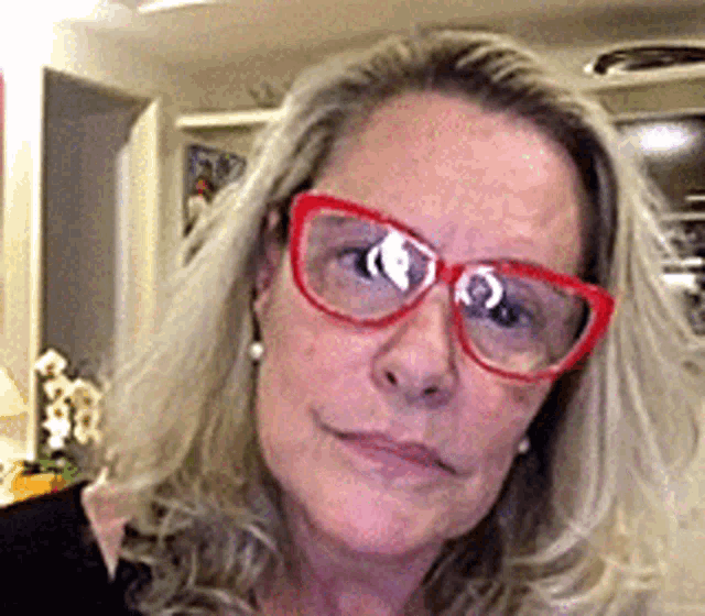 a woman wearing red glasses and earrings is smiling for the camera .