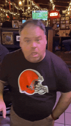 a man wearing a cleveland browns shirt stands in front of a television