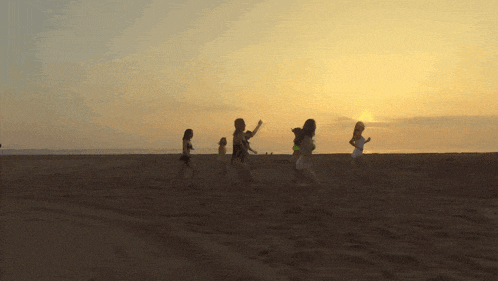 a group of young girls are running on a beach at sunset