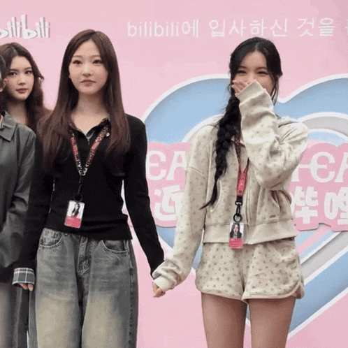 a group of girls standing in front of a pink heart that says bilibili