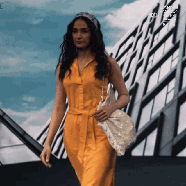 a woman in a yellow dress is walking in front of a building with lakme fashion week written on it