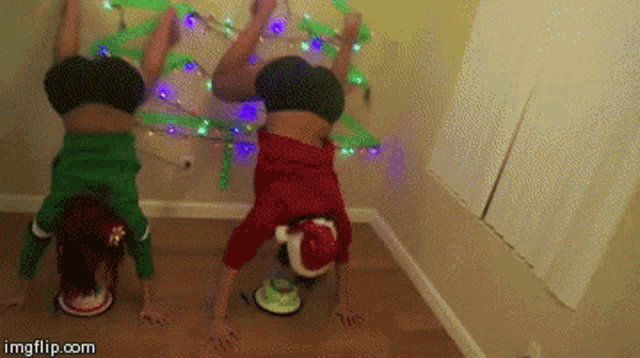 two people doing handstands in front of a christmas tree