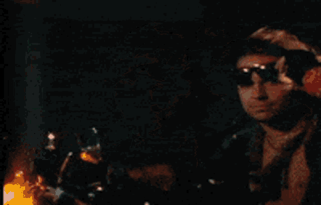 a man wearing sunglasses and a red wristband stands in a dark room