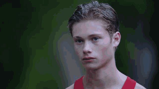 a young man wearing a red tank top looks to the side