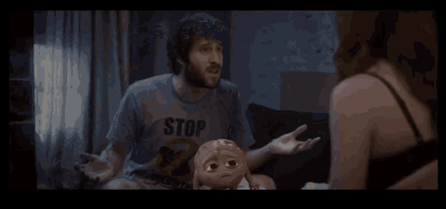 a man and a woman are sitting on a bed in a dark room . the woman is wearing a bra .