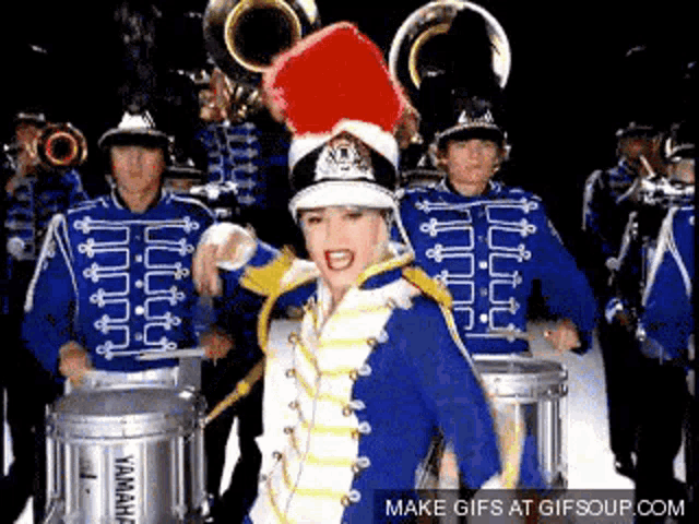 a woman in a parade uniform is standing in front of a marching band playing drums .