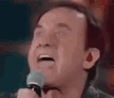 a man is singing into a microphone and making a funny face with his mouth open .