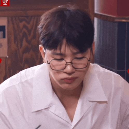 a young man wearing glasses and a white shirt looks down at something