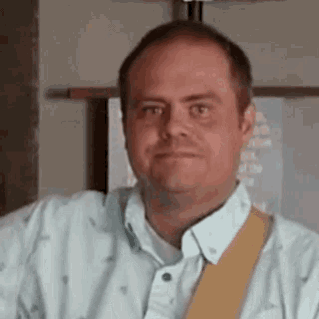 a man wearing a light blue shirt and a yellow tie is making a funny face .