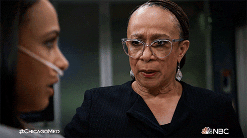 a woman wearing glasses is talking to another woman with a nbc logo in the background
