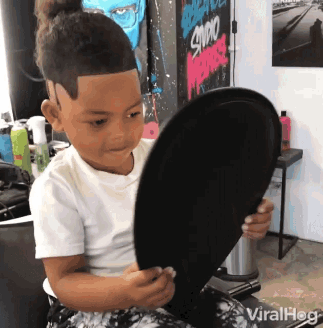 a young boy is looking at himself in a mirror with a sign that says studio on the wall behind him