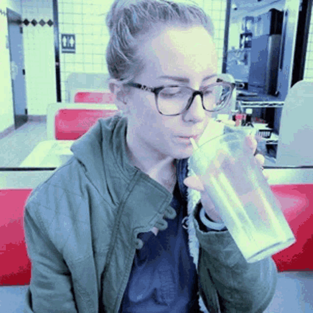 a woman wearing glasses is drinking from a clear glass with a straw