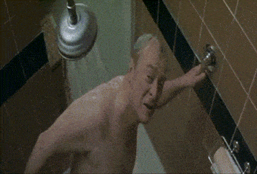 a shirtless man is taking a shower and adjusting the shower head