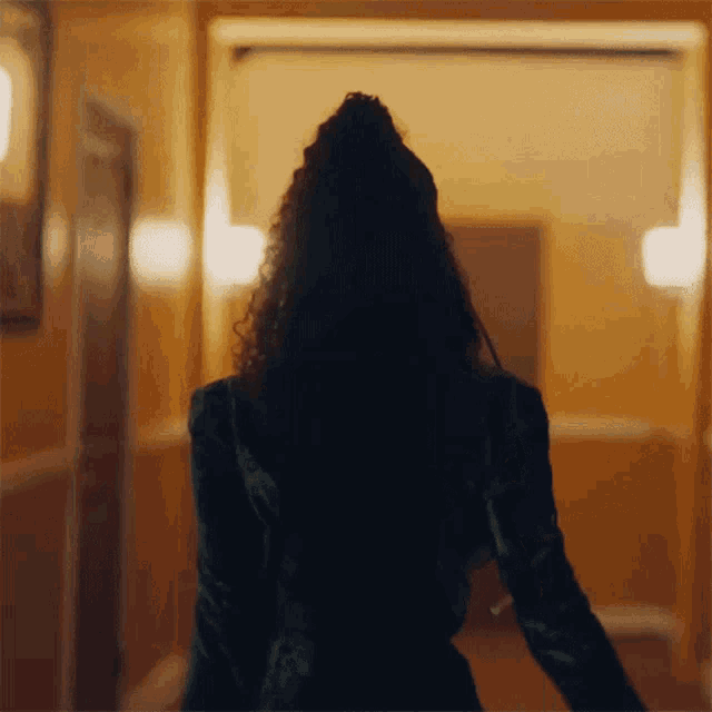 a woman in a green jacket is walking down a hallway in a dark room .