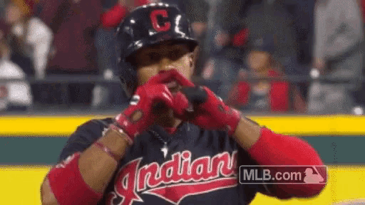 a baseball player is wearing a helmet and gloves and is making a heart shape with his hands .