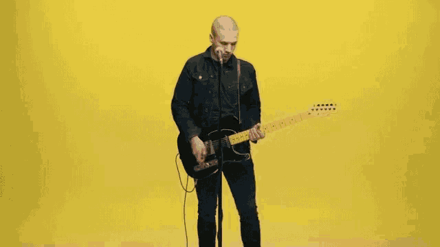 a man playing a guitar and singing into a microphone on a yellow background