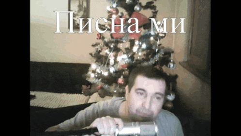 a man is holding a camera in front of a christmas tree with the words " писна ми " written above him
