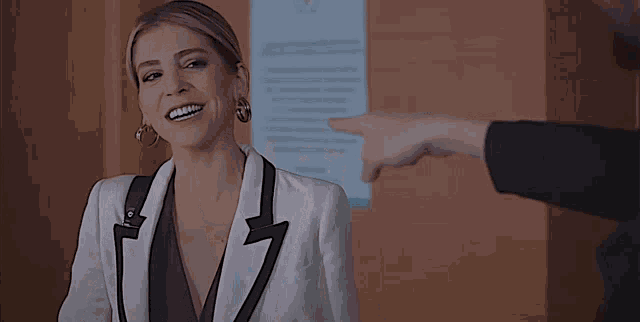 a woman in a white suit is smiling while standing in front of a wall .