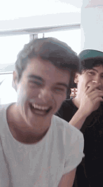 a man in a white shirt is laughing while another man covers his mouth