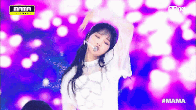 a woman in a white dress is performing on a stage with purple lights behind her and the words mama on the bottom