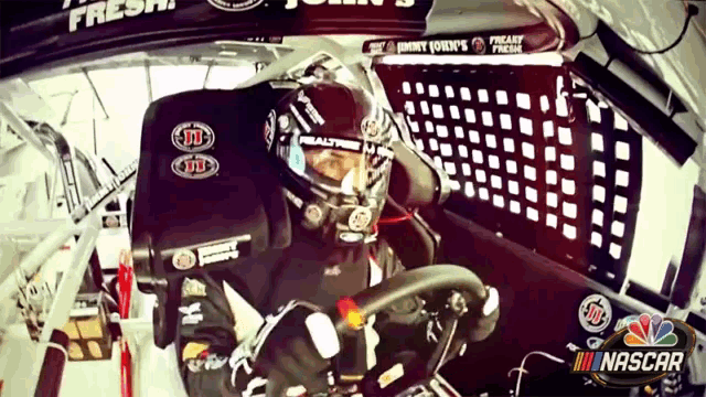 a man is sitting in a race car with a nascar logo in the corner