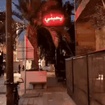 a red sign with arabic writing on it is lit up on a sidewalk