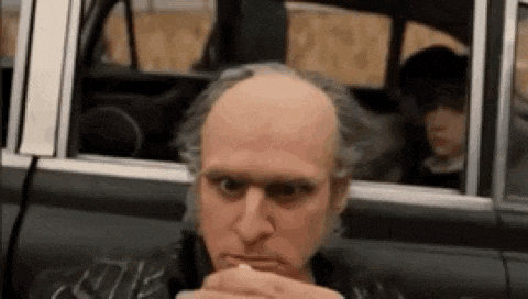 a bald man is sitting in a car eating a hamburger .