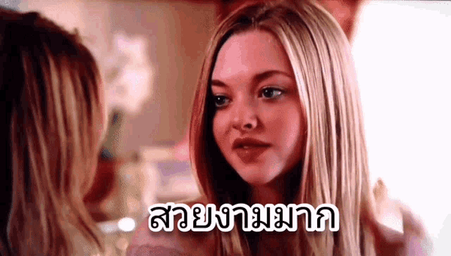 a woman is looking at herself in a mirror with the words " สวย งาม มาก " on the bottom